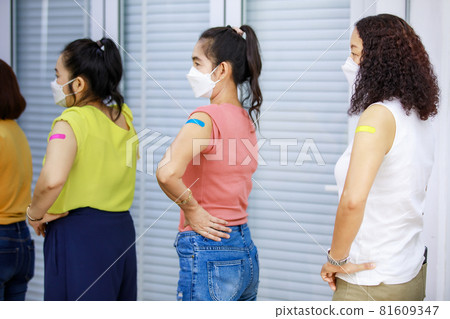 Three Asian female patients standing waiting in orderly straight line showing colorful plasters on shoulder after receiving Coronavirus Covid-19 vaccine injection shot in hospital already Three Asian female patients standing waiting in orderly straight line showing colorful plasters on shoulder after receiving Coronavirus Covid-19 vaccine injection shot in hospital already 81609347
