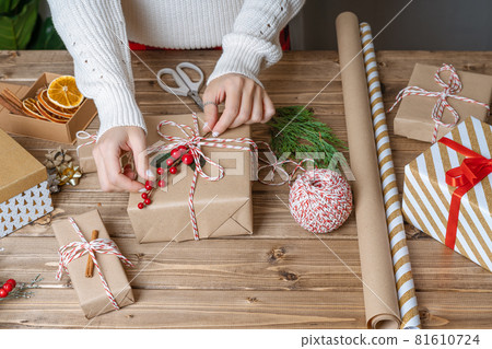 Woman s hands wrapping Christmas gift, close up. Unprepared presents on wooden background with decor elements and items, top view. Christmas or New year DIY packing Concept. Step by step. Woman s hands wrapping Christmas gift, close up. Unprepared presents on wooden background with decor elements and items, top view. Christmas or New year DIY packing Concept. Step by step. 81610724