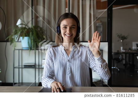 Head shot portrait smiling businesswoman in headphones waving hand Head shot portrait smiling businesswoman in headphones waving hand 81611285