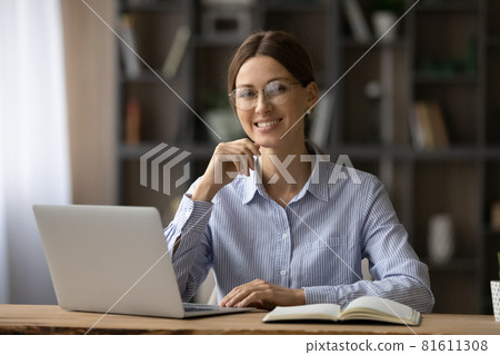 Head shot portrait smiling woman in glasses sitting at desk 81611308