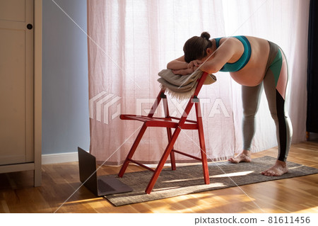 Pregnant woman doing inversion Standing Intense Spread Leg Prasarita Padottanasana yoga pose at home 81611456