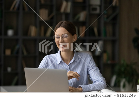 Laughing woman in glasses sitting at work desk with laptop 81613249