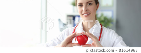 Smiling woman doctor holding red toy heart in her hands in clinic Smiling woman doctor holding red toy heart in her hands in clinic 81614965