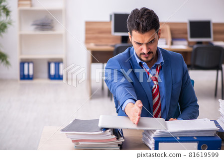 Young male employee unhappy with excessive work at workplace Young male employee unhappy with excessive work at workplace 81619599