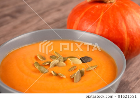 Closeup view on gray bowl with pumpkin cream soup toped with pumpkin seeds on wooden table background with copy space for text. Vegan food concept, homemade soup recipe. Autumn food. Selective focus Closeup view on gray bowl with pumpkin cream soup toped with pumpkin seeds on wooden table background with copy space for text. Vegan food concept, homemade soup recipe. Autumn food. Selective focus 81621551
