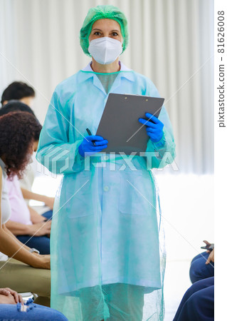 Caucasian female nurse wears full protection gears face mask rubber gloves lab coat and hat stand look at camera hold information paper board and pen in front patients line Caucasian female nurse wears full protection gears face mask rubber gloves lab coat and hat stand look at camera hold information paper board and pen in front patients line 81626008