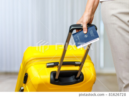 Close up shot of female hand holding Deutschland passport Coronavirus Covid-19 vaccination record card certificate and pull yellow trolley luggage bag to traveling abroad after lockdown quarantine 81626728