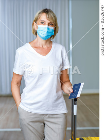 Portrait closeup shot of Caucasian senior female patient wears face mask hold blue Covid-19 vaccination record card passport and luggage after receive coronavirus vaccine and ready to travel abroad Portrait closeup shot of Caucasian senior female patient wears face mask hold blue Covid-19 vaccination record card passport and luggage after receive coronavirus vaccine and ready to travel abroad 81626747