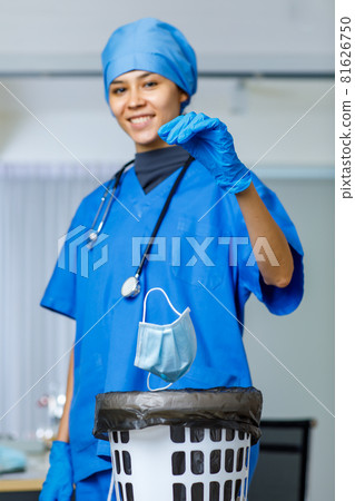 Portrait closeup shot of used surgical face mask dumped drop from happy pretty female freedom doctor hand in blue hospital suit hat with stethoscope smiling look at camera while covid pandemic end 81626750