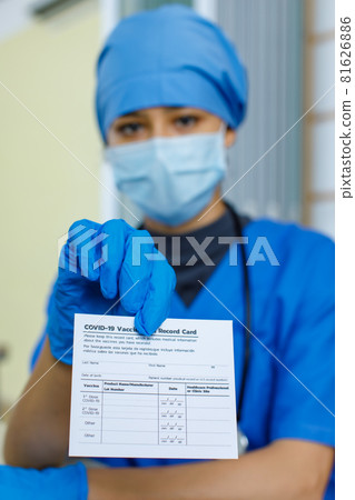 Closeup shot of Covid-19 vaccination record card certificate passport paper sent to patient by doctor wears blue hospital uniform face mask rubber gloves and stethoscope in blurred background Closeup shot of Covid-19 vaccination record card certificate passport paper sent to patient by doctor wears blue hospital uniform face mask rubber gloves and stethoscope in blurred background 81626886