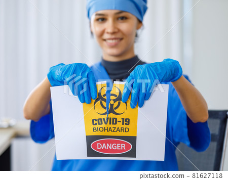 Yellow Covid-19 biohazard danger paper sign was torn apart by happy beautiful doctor in blue hospital uniform in blurred background when coronavirus pandemic has ended and normal life are back Yellow Covid-19 biohazard danger paper sign was torn apart by happy beautiful doctor in blue hospital uniform in blurred background when coronavirus pandemic has ended and normal life are back 81627118