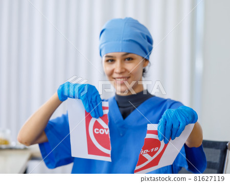 Red Covid-19 paper sign was torn apart by happy beautiful doctor in blue hospital uniform in blurred background when coronavirus pandemic has ended and normal life and business open safety Red Covid-19 paper sign was torn apart by happy beautiful doctor in blue hospital uniform in blurred background when coronavirus pandemic has ended and normal life and business open safety 81627119