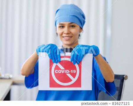 Red Covid-19 paper sign was torn apart by happy beautiful doctor in blue hospital uniform in blurred background when coronavirus pandemic has ended and normal life and business open safety Red Covid-19 paper sign was torn apart by happy beautiful doctor in blue hospital uniform in blurred background when coronavirus pandemic has ended and normal life and business open safety 81627121