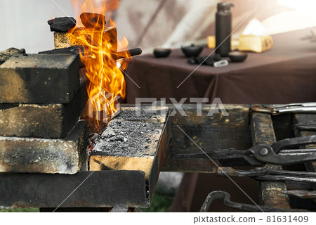Different blackened metal tools of the blacksmith lie in front of burning fire Different blackened metal tools of the blacksmith lie in front of burning fire 81631409