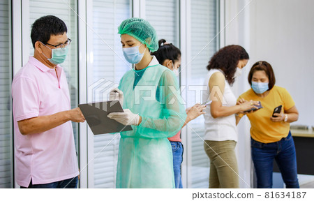 Young female nurse in full hazard protection uniform holding paper board asking personal information from senior male patient while others using application in smartphone in blurred background Young female nurse in full hazard protection uniform holding paper board asking personal information from senior male patient while others using application in smartphone in blurred background 81634187