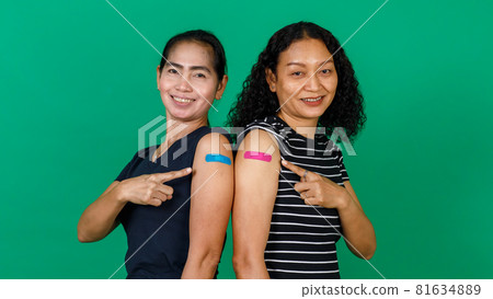 Two middle aged Asian women showing their arms with bandage patch showing they got vaccinated for Covid 19 virus on green background. Concept for Covid 19 vaccination Two middle aged Asian women showing their arms with bandage patch showing they got vaccinated for Covid 19 virus on green background. Concept for Covid 19 vaccination 81634889