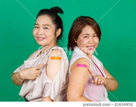 Two middle aged Asian women showing their arms with bandage patch showing they got vaccinated for Covid 19 virus on green background. Concept for Covid 19 vaccination Two middle aged Asian women showing their arms with bandage patch showing they got vaccinated for Covid 19 virus on green background. Concept for Covid 19 vaccination 81634958