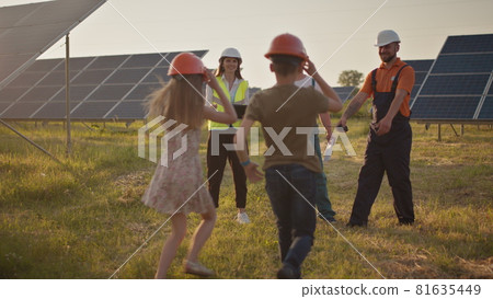Three solar energy specialists at a solar power facility. Two small children run to their parents who are at work. A solar power plant employee with children at work smiling at the camera. Happy 81635449