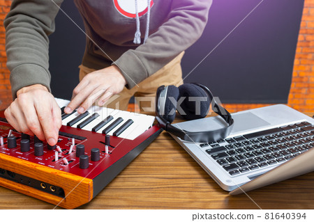 male happy DJ playing red analog synthesizer keyboard with laptop computer and headphone on desk male happy DJ playing red analog synthesizer keyboard with laptop computer and headphone on desk 81640394