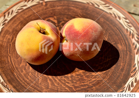 Two ripe peaches on a clay plate on the table. 81642925