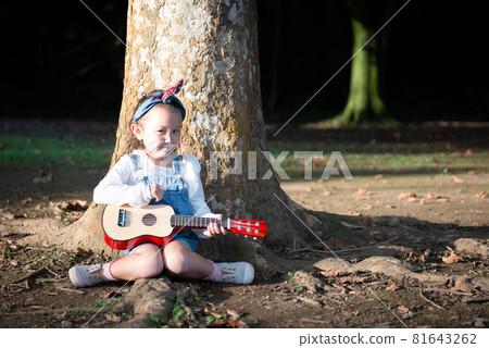 Girl sitting on a tree trunk and pulling a guitar Girl sitting on a tree trunk and pulling a guitar 81643262