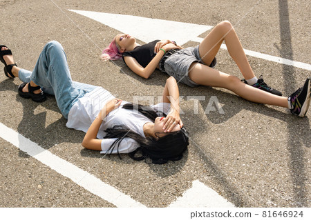 two teenage girls have fun lying on an empty road parallel to the markings two teenage girls have fun lying on an empty road parallel to the markings 81646924