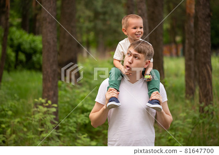 Happy funny kid riding on dads shoulders. Caucasian dad and son playing together 81647700