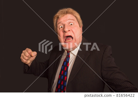 Studio shot of angry senior businessman with fist raise against dark background Studio shot of angry senior businessman with fist raise against dark background 81656422