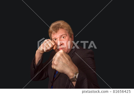 Studio shot of angry senior businessman with fist raise against dark background Studio shot of angry senior businessman with fist raise against dark background 81656425