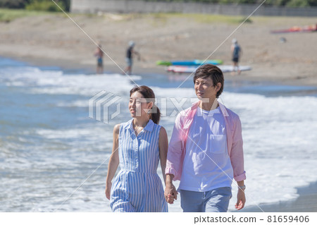 A couple taking a walk hand in hand at the beach in summer 81659406