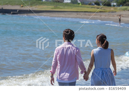 A couple taking a walk hand in hand at the beach in summer 81659409