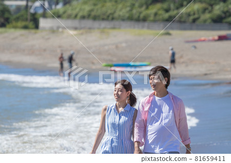 A couple taking a walk hand in hand at the beach in summer 81659411