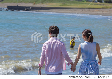 A couple taking a walk hand in hand at the beach in summer 81659414