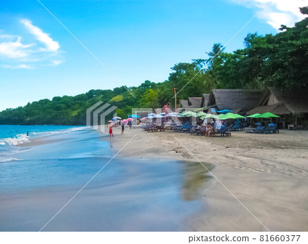 Amed, Bali, Indonesia. The volcano Gunung Agung dominates the horizon as a wave breaks over the black sand beach 81660377