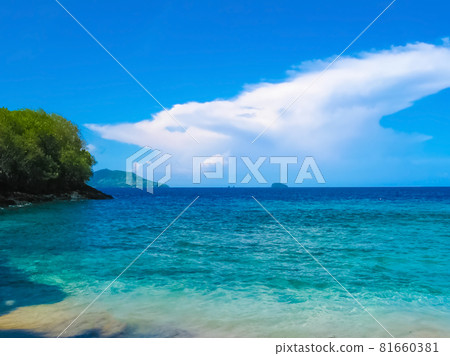 Amed, Bali, Indonesia. The volcano Gunung Agung dominates the horizon as a wave breaks over the black sand beach 81660381
