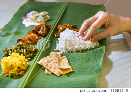 Person enjoying Indian banana leaf rice consisting mutton curry, squid, prawn, papadam and various vegetables 81661349