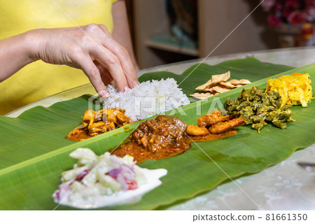 Person enjoying Indian banana leaf rice consisting mutton curry, squid, prawn, papadam and various vegetables Person enjoying Indian banana leaf rice consisting mutton curry, squid, prawn, papadam and various vegetables 81661350