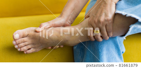 Woman sitting on sofa using hand to hold leg and feeling pain, suffer, hurt and tingling. Concept of Guillain barre syndrome and numb hands disease effect 81661879