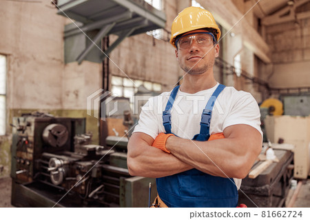 Athletic male builder in construction helmet standing in workshop Athletic male builder in construction helmet standing in workshop 81662724