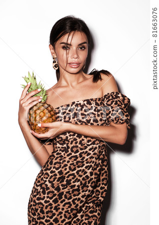 Beautiful sexy woman with pineapple in hands in a leopard dress and earrings, with classic smokey makeup and a fashionable hairstyle. Beauty face. Beautiful sexy woman with pineapple in hands in a leopard dress and earrings, with classic smokey makeup and a fashionable hairstyle. Beauty face. 81663076