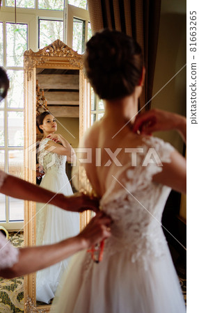 the bride is helped to put on a dress and fastened the corset. 81663265