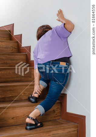 Woman loses control and cannot walk on stairs, she stops and hold her legs for support and rest with feel tingling. Concept of Guillain barre syndrome and numb legs disease or vaccine side effect 81664556