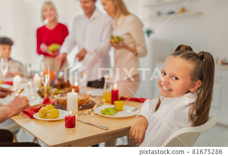Adorable happy girl sitting at festive table, celebrating traditional holiday with her big family at home, copy space 81675286