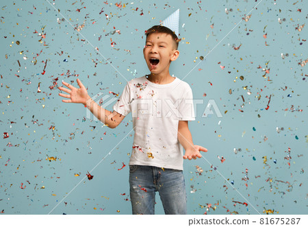 Birthday Party. Happy Asian Boy Wearing B-Day Hat Standing Under Falling Confetti Birthday Party. Happy Asian Boy Wearing B-Day Hat Standing Under Falling Confetti 81675287
