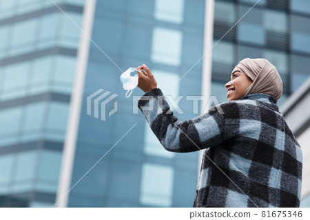 Glad smiling pretty black woman in hijab and coat holds medical mask in hand and enjoys freedom outdoor Glad smiling pretty black woman in hijab and coat holds medical mask in hand and enjoys freedom outdoor 81675346