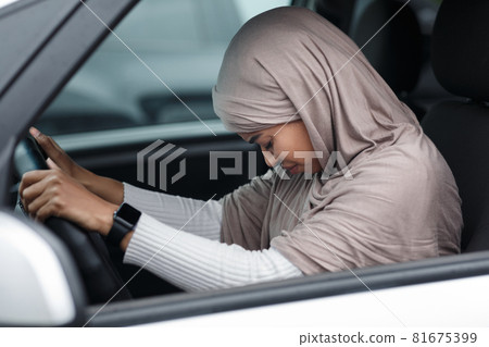 Upset afro american lady in hijab driving car, bowed head and regrets about accident, suffers from pain after incident Upset afro american lady in hijab driving car, bowed head and regrets about accident, suffers from pain after incident 81675399
