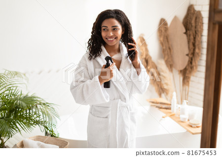 African American Woman Spraying Hairspray Moisturizing Hair In Bathroom 81675453
