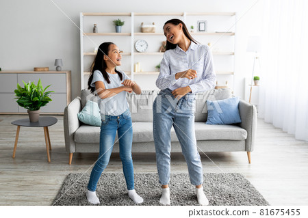Full length of asian mother dancing to music with her cute daughter at home, having fun together 81675455