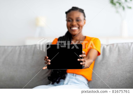 Cheery Afro woman showing tablet pc with blank screen, buying goods in internet store from home, mockup 81675761