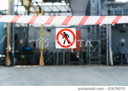 The poster No trespassing is allowed on a red and white ribbon fencing the passage against the background of the pipes of the power plant. 81676070